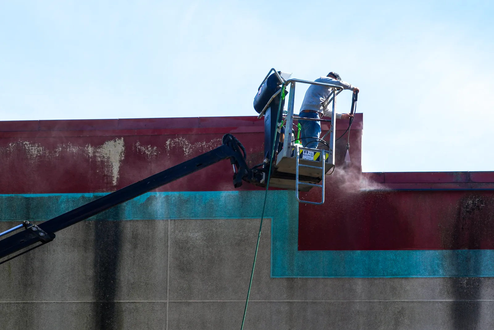 Technician pressure washing a commercial building facade from a boom lift